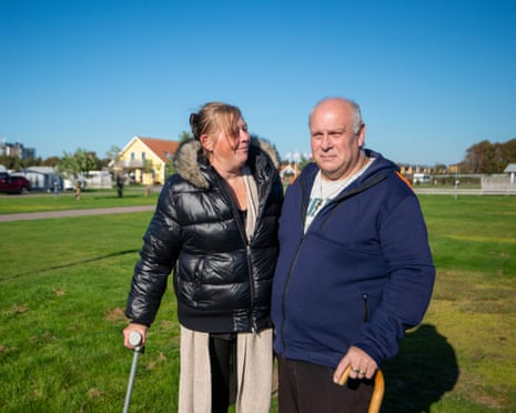 Mark Smith and his wife Petra stand outdoors on grass, each holding a walking stick