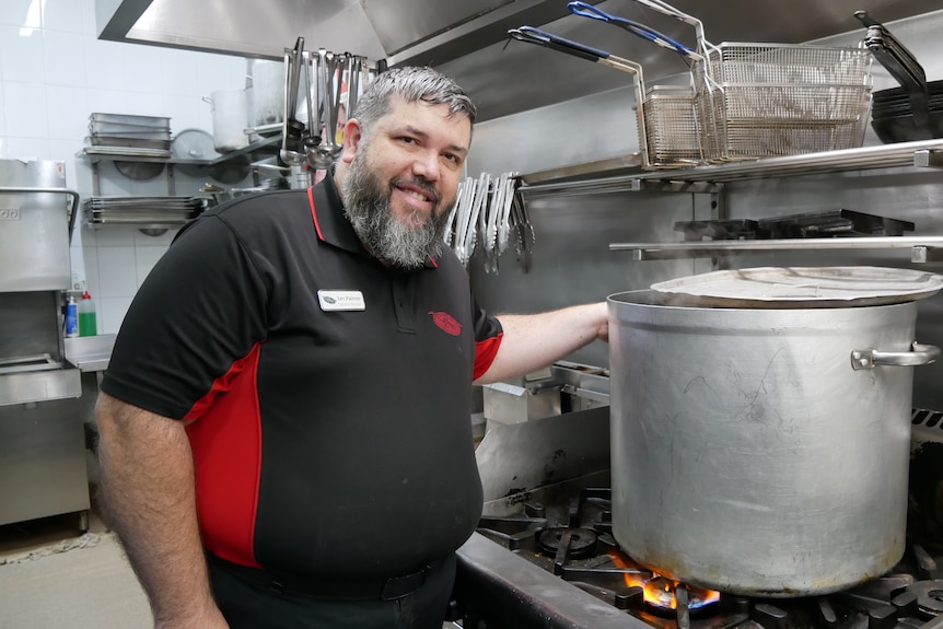 A man with his hand on a pot in a kitchen